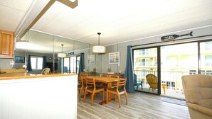 Een zithoek met een houten tafel en stoelen, een spiegel en uitzicht op een gebouw door een glazen deur.