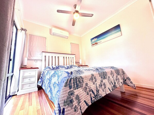 A bedroom with a bed, a ceiling fan, an air conditioning unit, a nightstand, a dresser, and a painting on the wall. - Ocean Views, canoeing, swimming, Fishing, 4x4 touring. (Fraser Island)