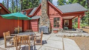 Une cabane rouge avec une cheminée en pierre, un patio couvert avec des meubles en bois et un parasol vert.