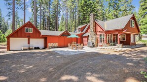 Une cabane à deux étages avec une cheminée en pierre, un patio couvert avec des meubles d’extérieur et un garage.
