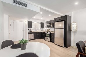 Une cuisine moderne avec des meubles noirs, des appareils en acier inoxydable et une table à manger blanche.