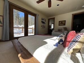 Une chambre avec un grand lit, une tête de lit en bois, une porte-fenêtre coulissante donnant sur un balcon et une vue sur un paysage enneigé.