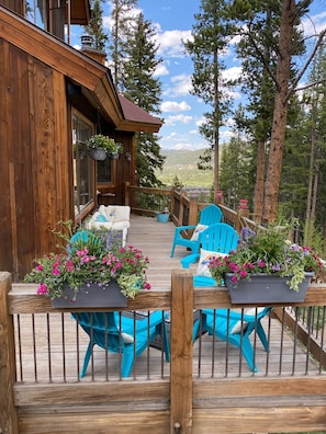 A wooden deck with blue chairs and planters with flowers, overlooking a forested area.