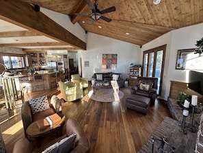 A spacious living room with wooden flooring, a ceiling fan, a fireplace, and a kitchen area with wooden cabinets and a dining table.