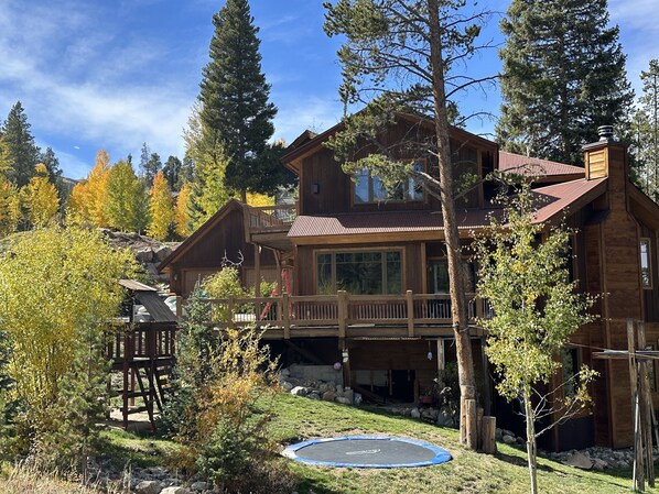 Une cabane en bois dotée d’un balcon, entourée d’arbres et agrémentée d’un trampoline dans la cour.