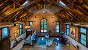 A spacious loft with exposed wooden beams, a large stained glass window, and a cozy seating area with sofas and a coffee table. - Luxurious, Converted Church Ideal for Large Groups near RiNo District, Sleeps 22 (Denver)