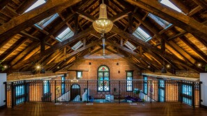 A spacious loft with exposed wooden beams, a large chandelier, and a brick wall with stained glass windows. - Luxurious, Converted Church Ideal for Large Groups near RiNo District, Sleeps 22 (Denver)