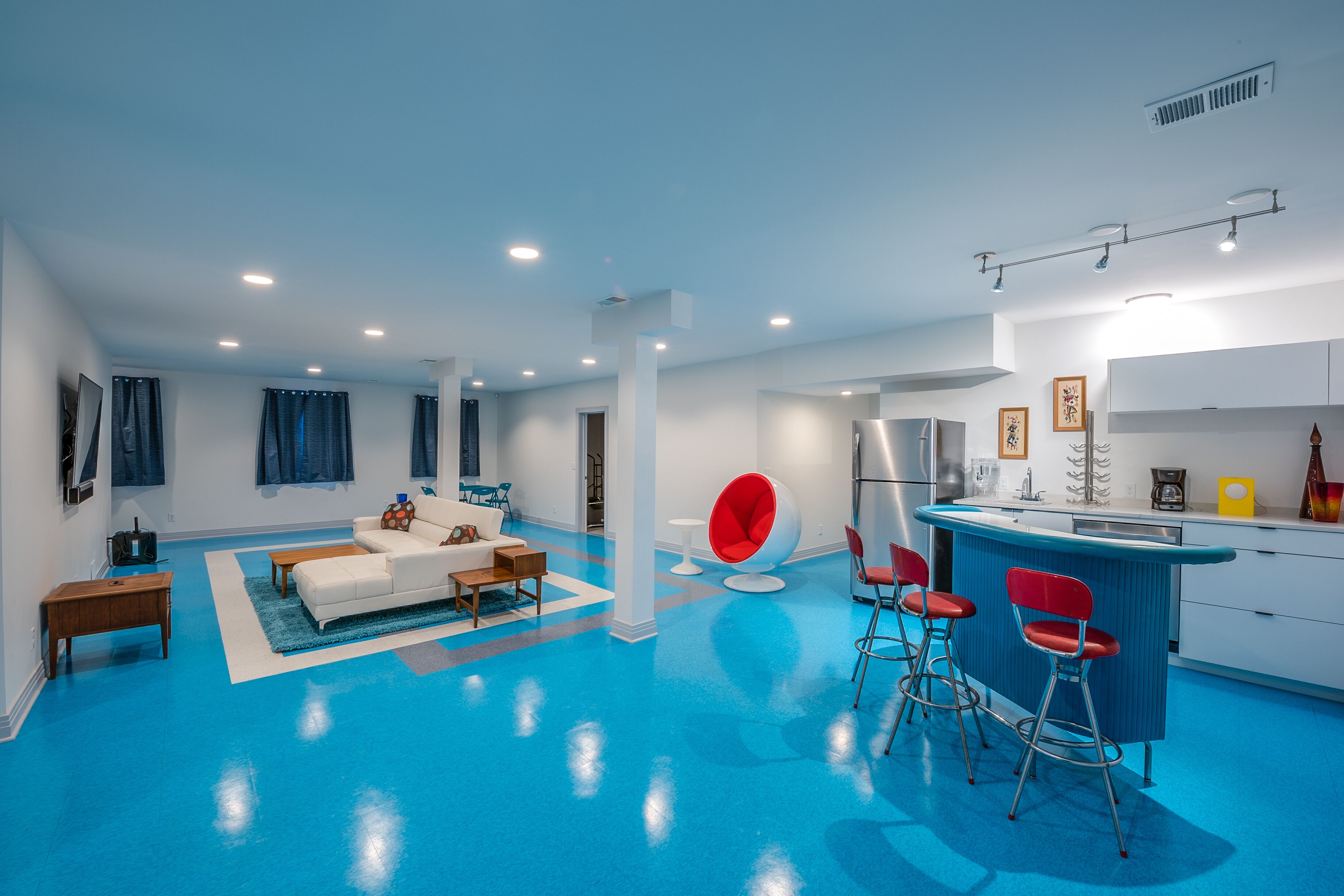 Una sala moderna con piso azul, sofá blanco y sillas rojas.