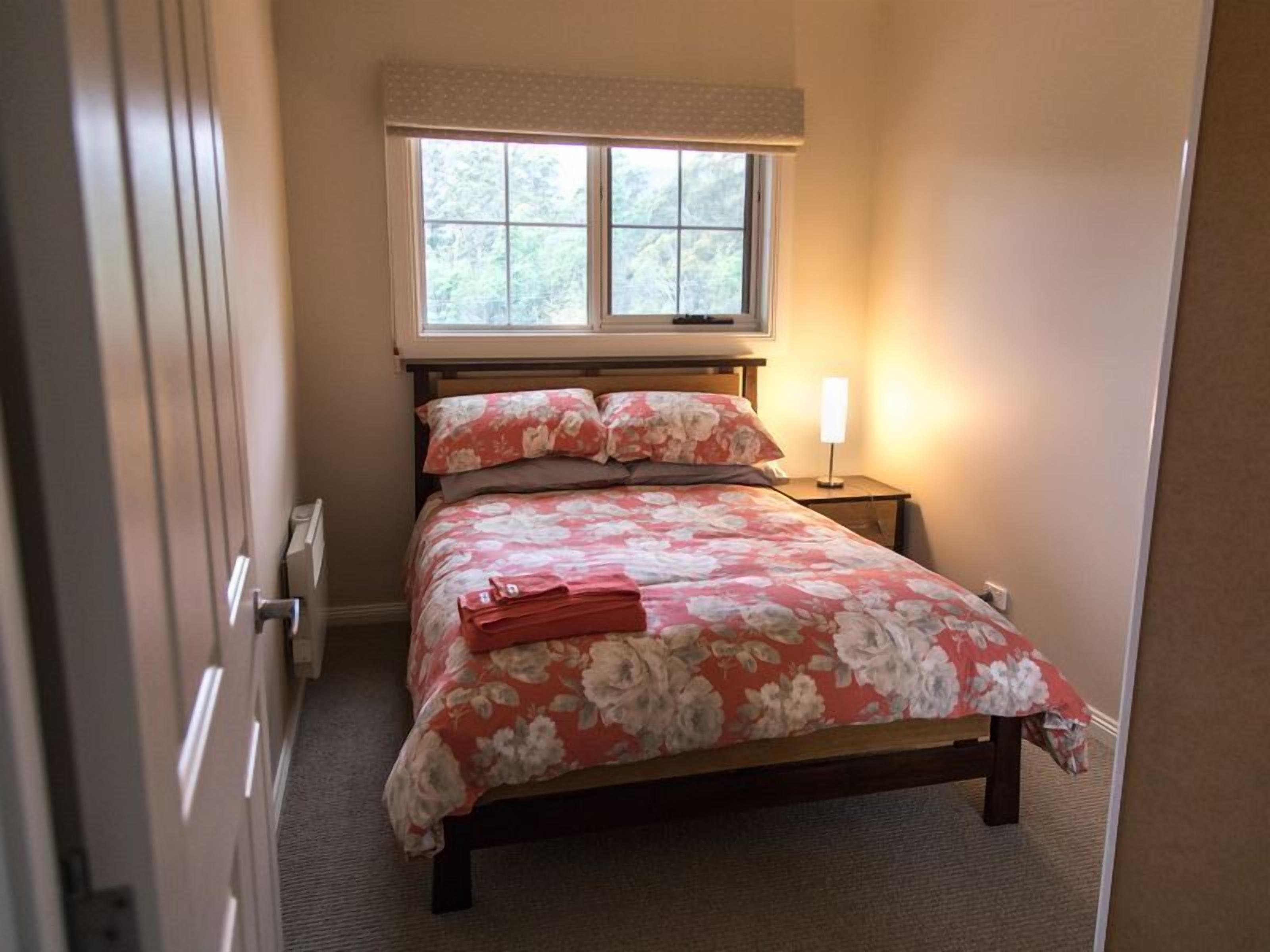 Un dormitorio con una cama, una ventana, una mesita de noche y una lámpara.