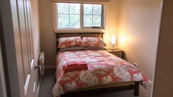 Un dormitorio con una cama, una ventana, una mesita de noche y una lámpara.