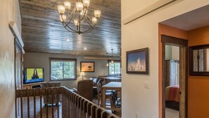 A wooden staircase leading to a living area with a television, a chandelier, and framed artwork.