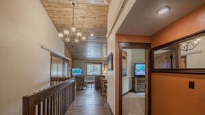 A hallway with wooden flooring, a chandelier, and a television in the background.