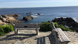 Een bank en picknicktafel op een stenen terras met uitzicht op een rotsachtige kustlijn en de oceaan op de achtergrond.