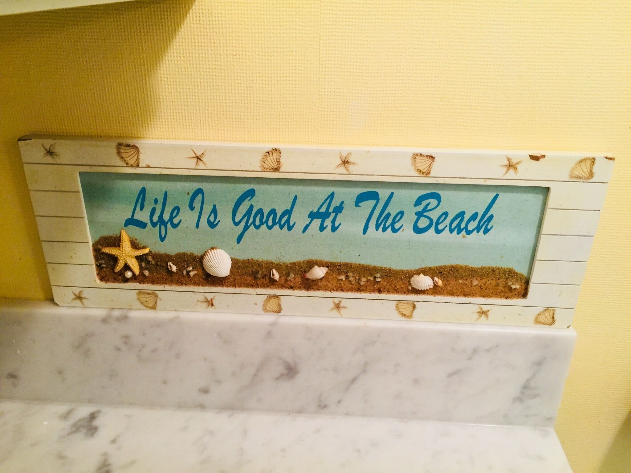 A decorative sign with the text "Life Is Good At The Beach" and a beach scene illustration.