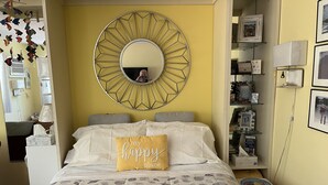 Een keurig opgemaakt slaapkamer met een bed, een nachtkastje, een spiegel en een muur versierd met ingelijste foto’s en een decoratief visobject.