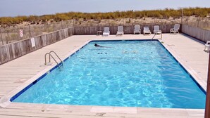 Une piscine rectangulaire avec une terrasse en bois, entourée d’une clôture et de végétation typique des zones côtières.
