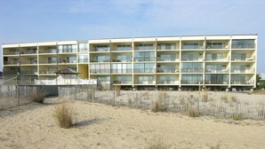 Un hôtel à plusieurs étages doté de balcons, une plage de sable en premier plan et un ciel dégagé.