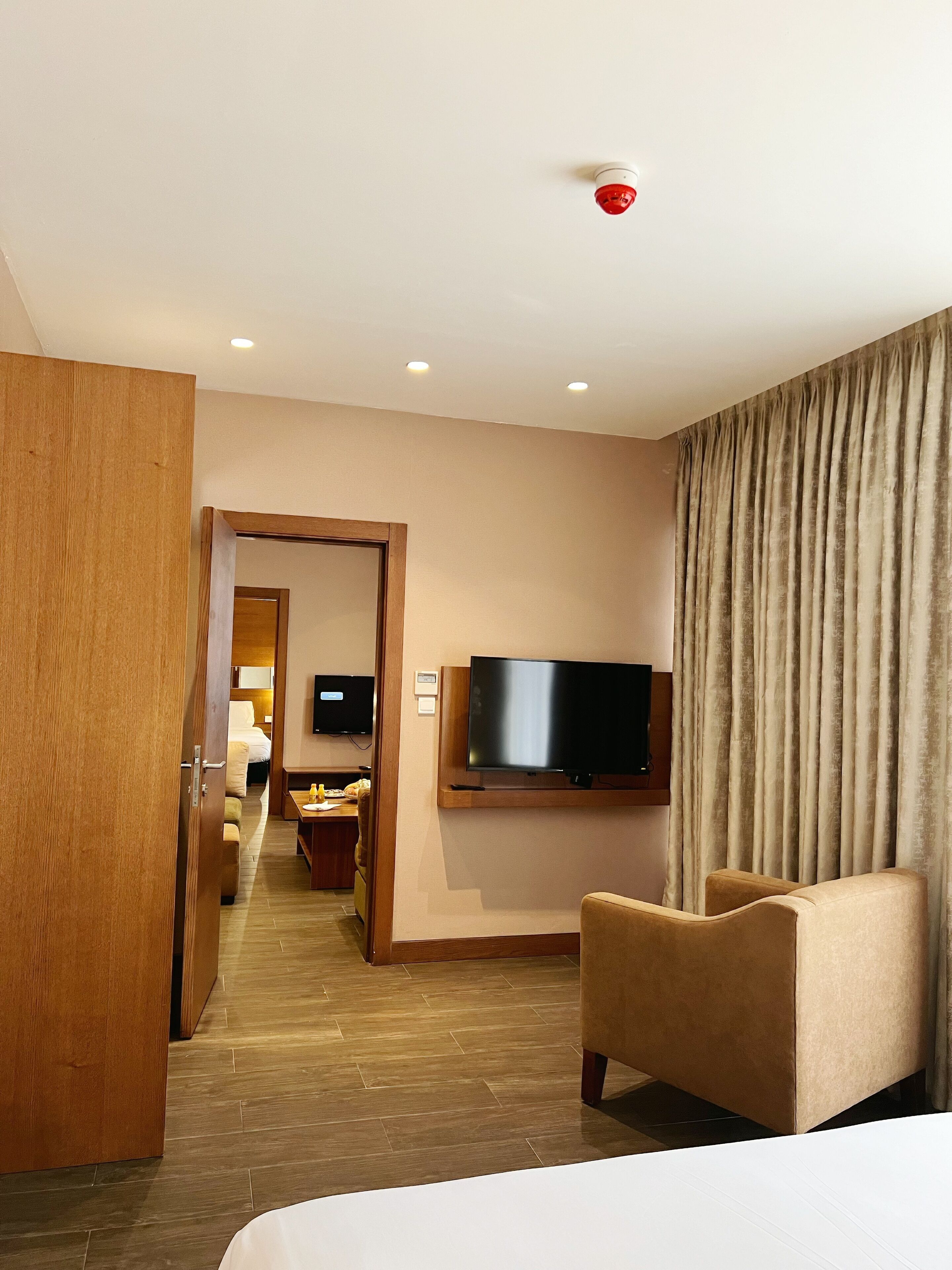 A hotel room with a bed, a TV mounted on the wall, a wooden door, and a view of the hallway.