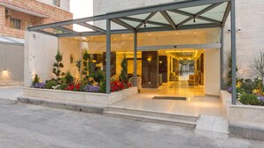A hotel entrance with a glass facade, a covered outdoor area, and a landscaped garden with various plants. - The Seventh Star Hotel Suites (Amman)