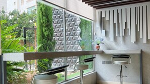A modern interior with two bar stools, a geometric wall design, and a view of greenery outside. - The Seventh Star Hotel Suites (Amman)