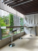 Un interior moderno con dos taburetes de bar, un diseño geométrico en la pared y vistas al exterior con vegetación.