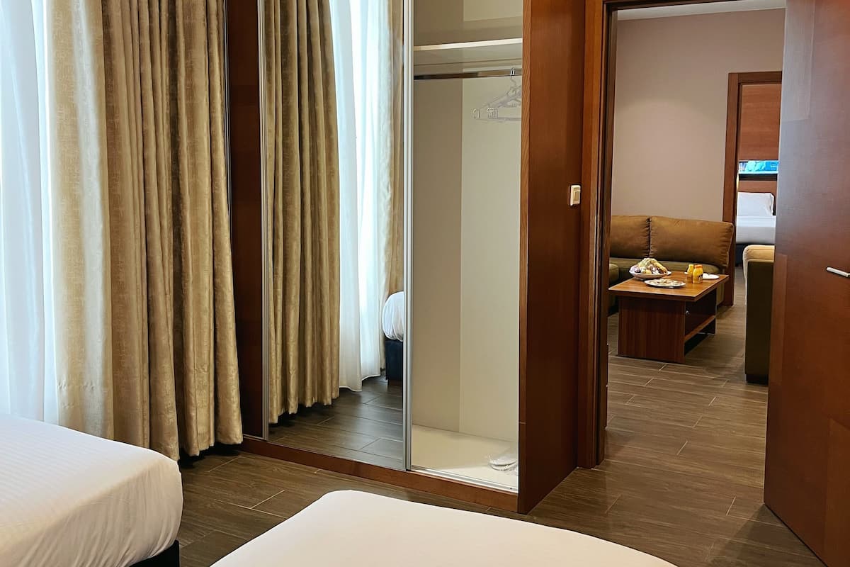 Habitación de hotel con dos camas, un armario, un espejo y una zona de comedor con mesa y sillas.