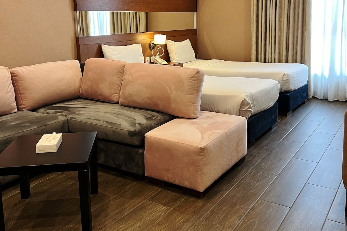 Habitación de hotel con sofá, cama, mesita de noche y lámpara.