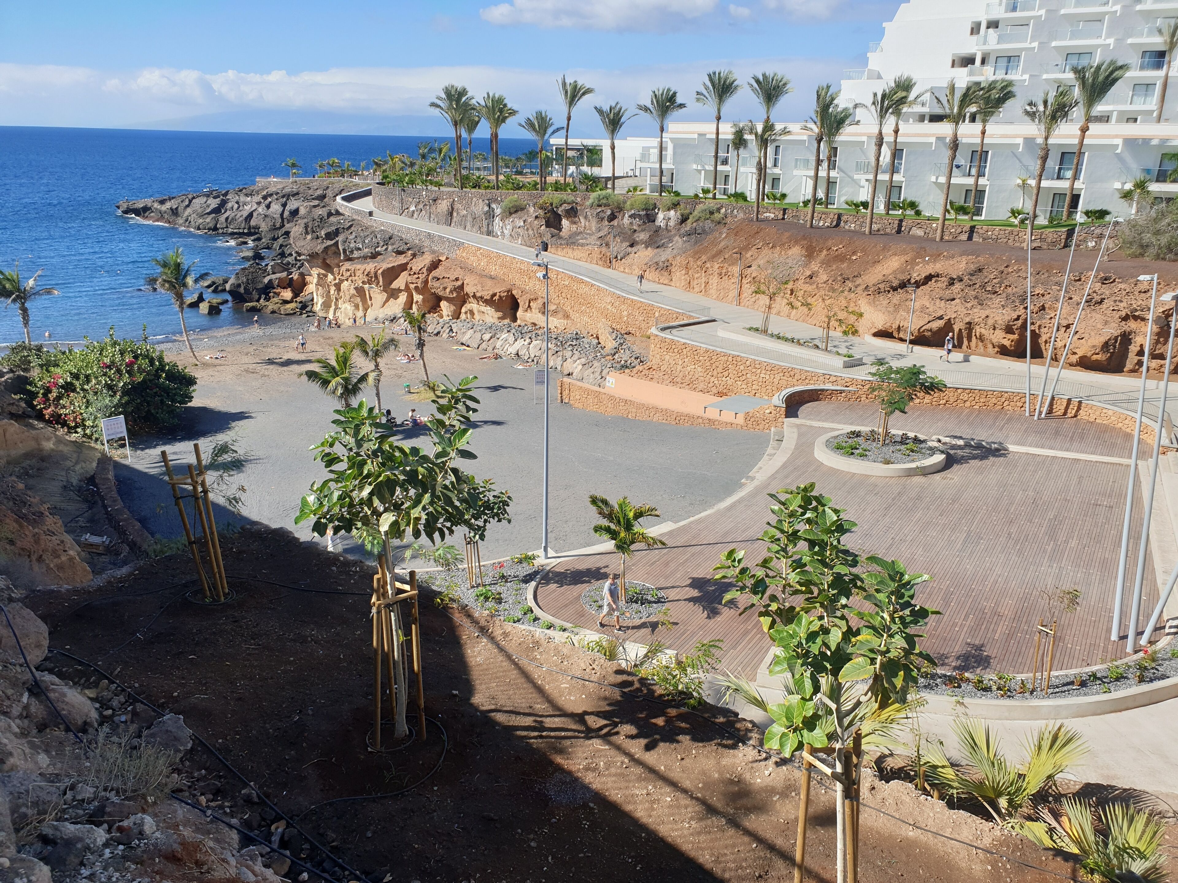 A coastal resort with a paved walkway, palm trees, and a view of the ocean.