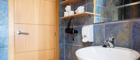 A bathroom with a wooden door, a white sink, a mirror, and a shelf with toiletries.