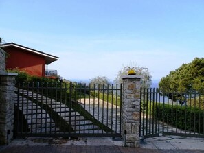 A gated entrance with a stone pillar and a metal gate, leading to a red building with a balcony.