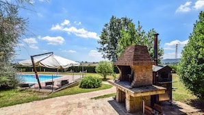 En baghave med en murstensgrill, swimmingpool og en overdækket patio.