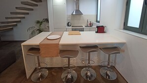 Una cocina moderna con una isla central, taburetes de bar, una campana extractora de acero inoxidable y una ventana con vistas.
