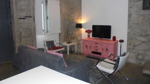 Una sala de estar con pared de piedra, un aparador rosa, un televisor de pantalla plana y un sofá gris.