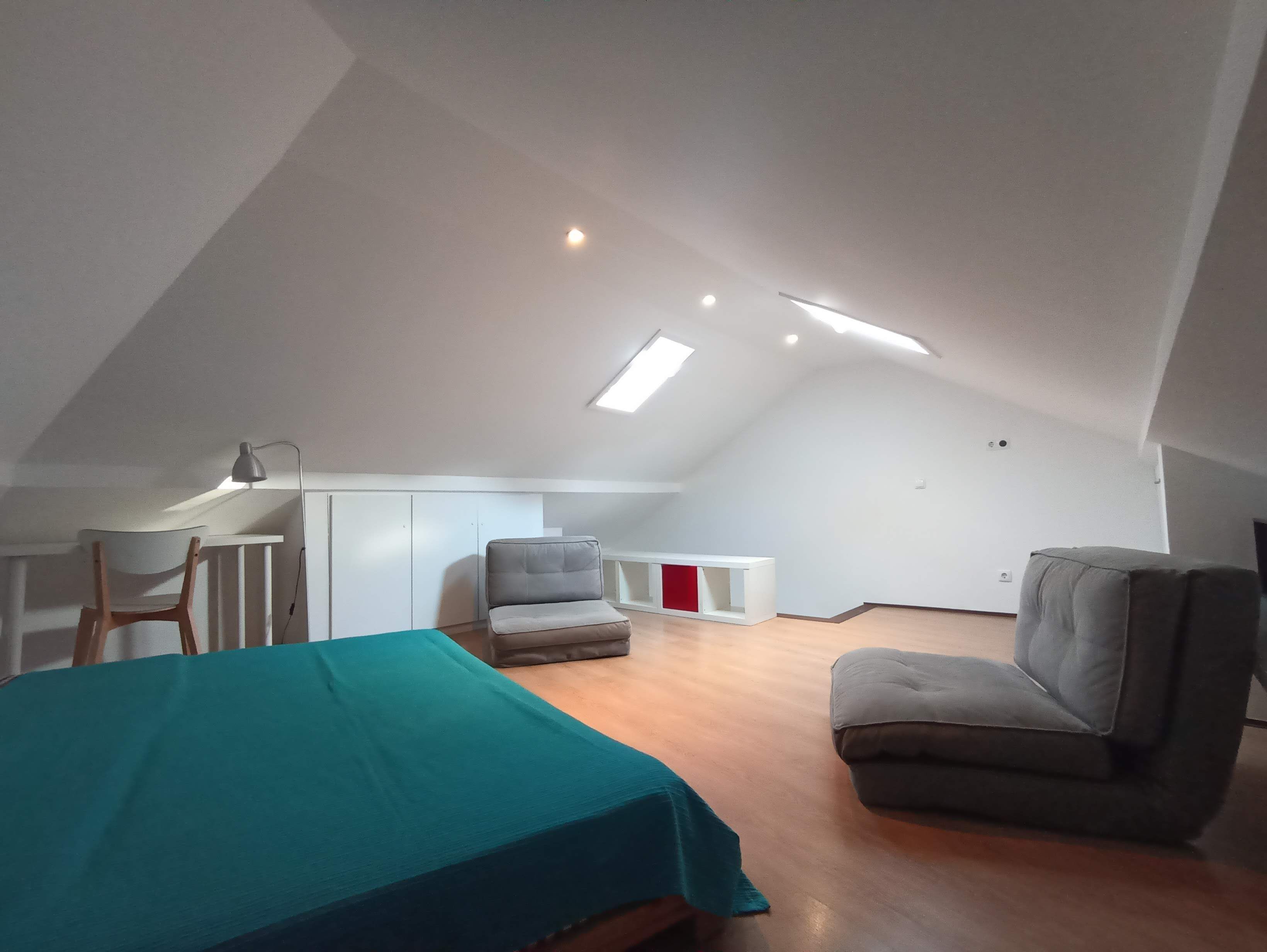 Une chambre spacieuse située dans les combles, avec un lit, un bureau et deux chaises.