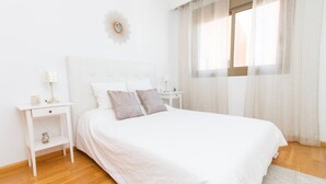 A neatly arranged bedroom with a large bed, a bedside table, a nightstand, and a window with sheer curtains. - Orient Express Apartment - In The Station (Málaga)