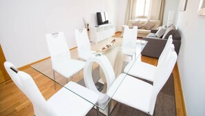 A modern living room with a glass dining table, white chairs, a sofa, and a TV. - Orient Express Apartment - In The Station (Málaga)