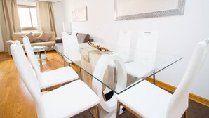 A modern dining area with a glass table and white chairs, a sofa, and a decorative mirror on the wall. - Orient Express Apartment - In The Station (Málaga)