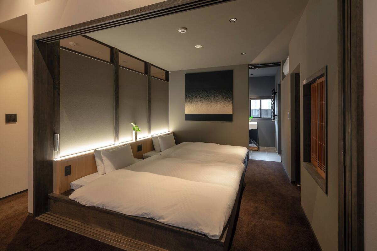 A modern hotel room with a large bed, a nightstand, a wall-mounted TV, and a sliding door leading to a balcony.