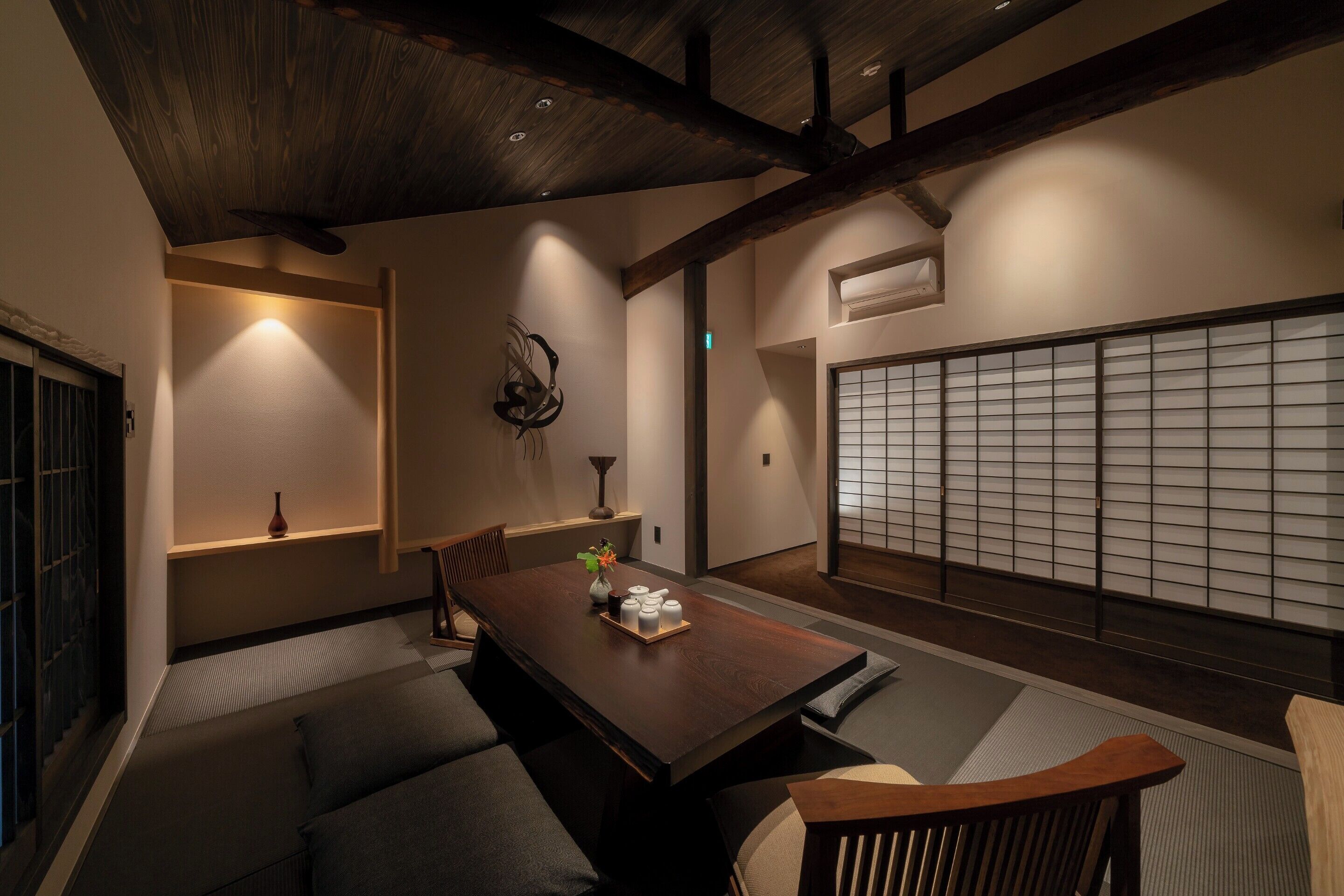 Ein traditioneller japanischer Raum mit Tatami-Boden, einem niedrigen Holztisch mit einer Vase und einer Tablett voller Gegenstände, sowie einem Shoji-Bildschirm im Hintergrund.