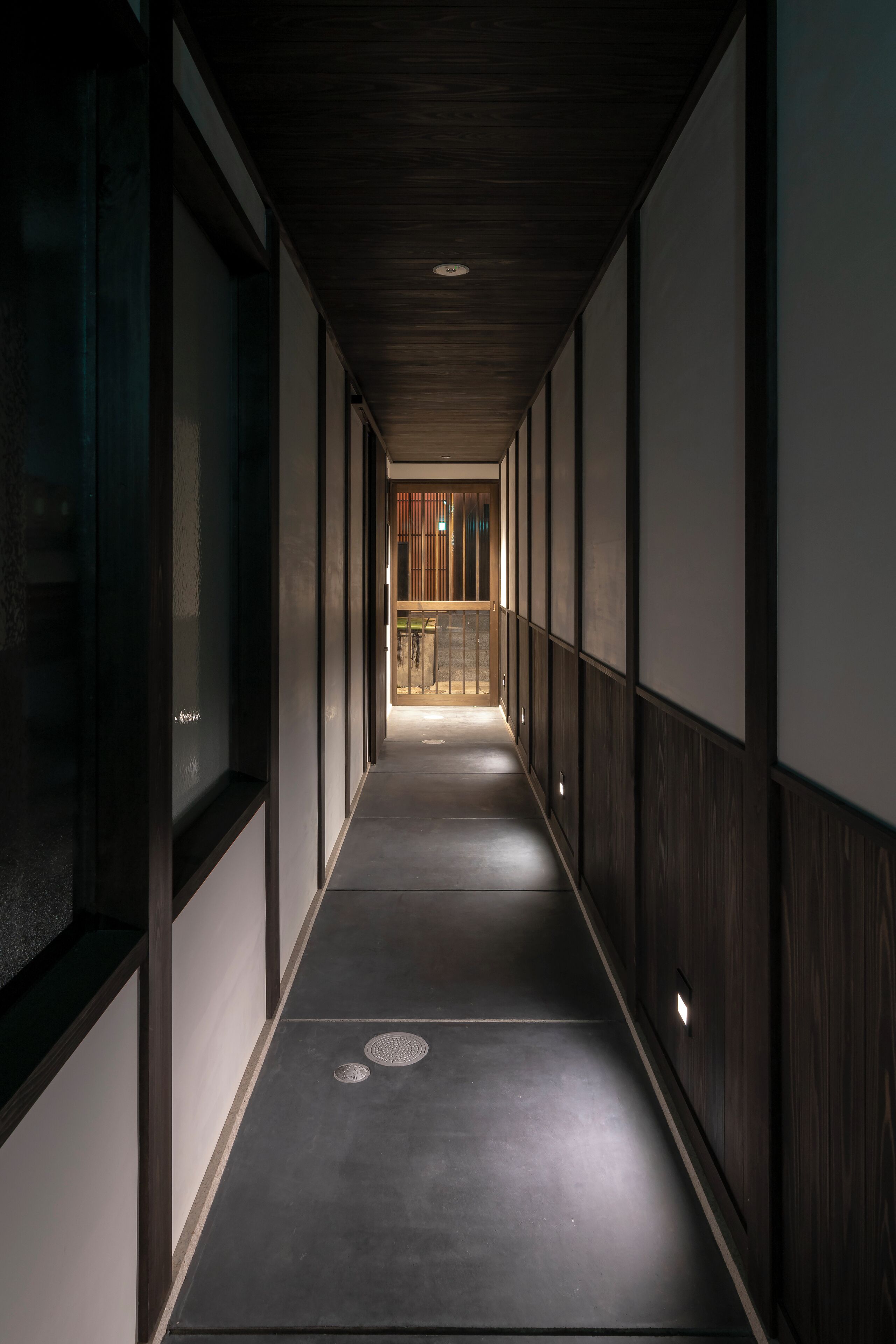 A corridor with wooden paneling and a dark floor, leading to a room with a wooden door and a visible interior.