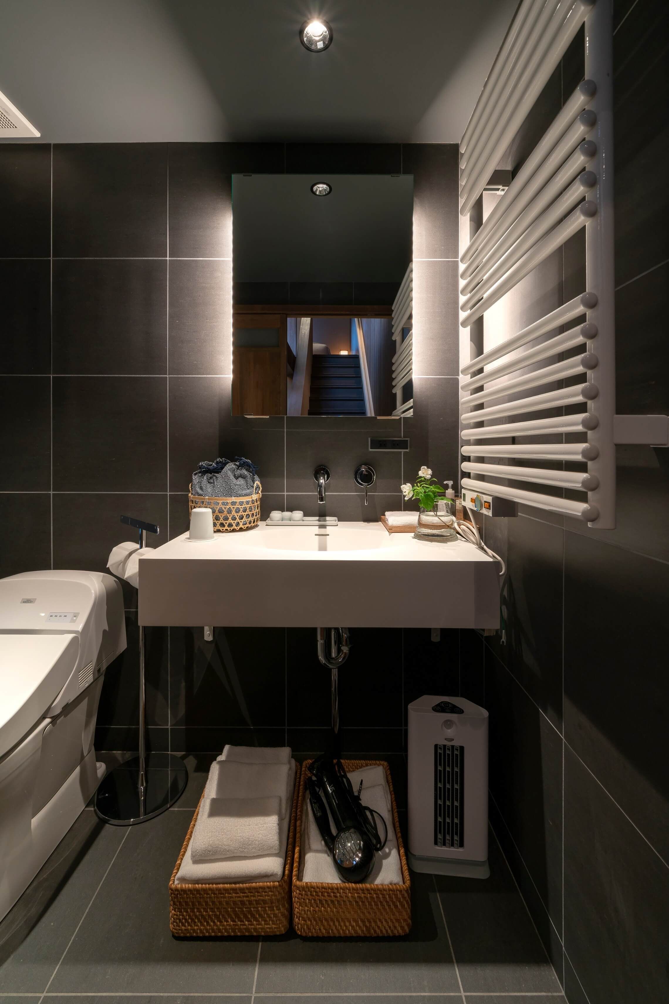 A modern bathroom with a large sink, towel racks, a heated towel rail, a small heater, and a basket with towels.