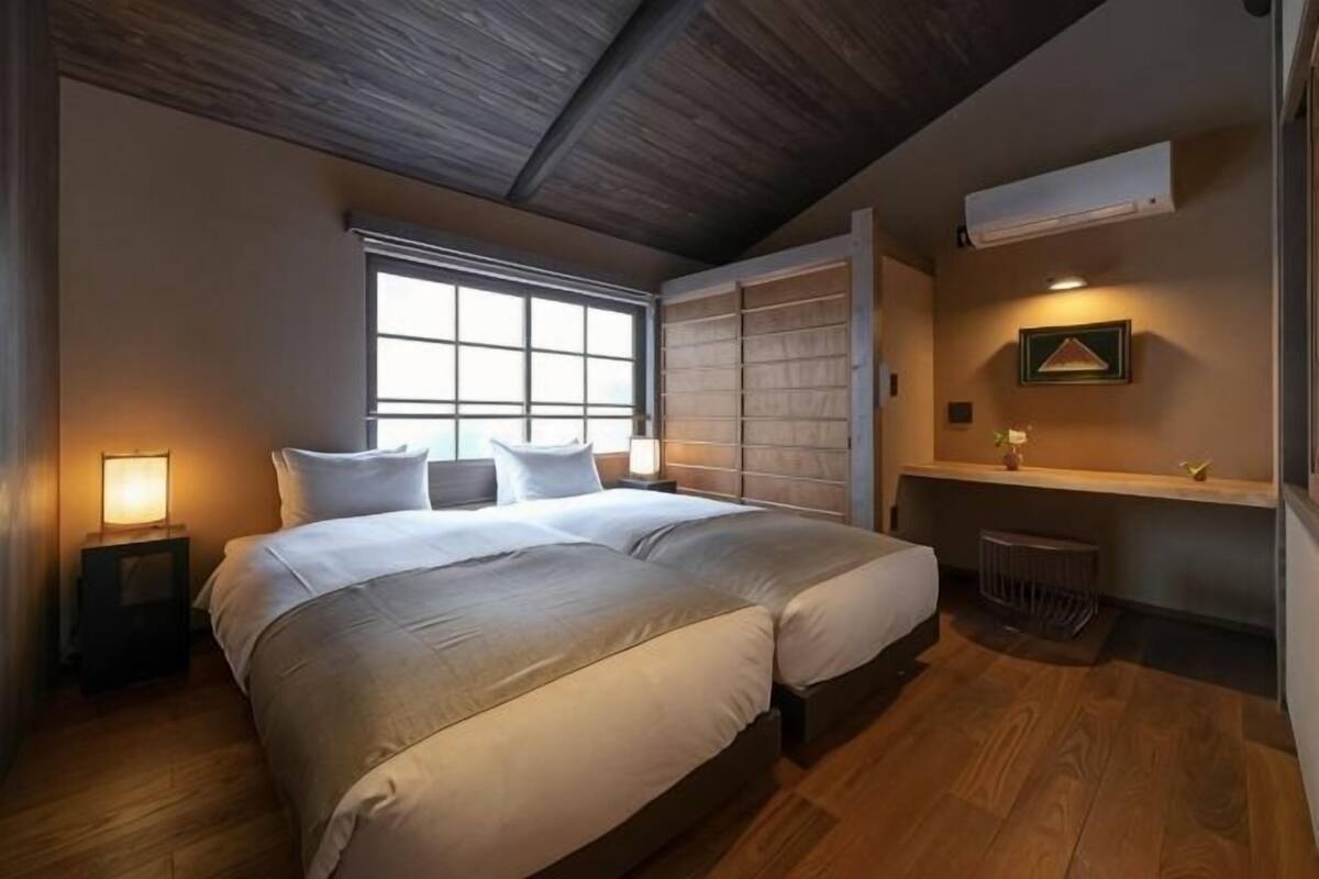 A bedroom with a large bed, a window, a bedside table with a lamp, a small shelf, and a radiator.