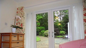 A room with a sliding glass door leading to a garden, wicker furniture, and a striped sofa. - Lily cottage In An Idyllic Riverside Location, Lake District Nation Park. (Selside Kendal,)