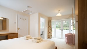 A bedroom with a bed, a bedside table, a mirror, a door with hooks, and a view of an outdoor area through a glass door. - Lily cottage In An Idyllic Riverside Location, Lake District Nation Park. (Selside Kendal,)