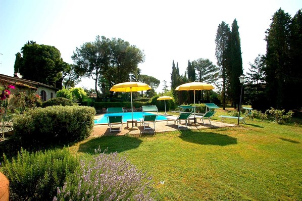 A backyard with a swimming pool, green lounge chairs, and yellow umbrellas.