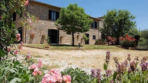 Edifici de pedra amb una entrada central, envoltat d'un jardí ben cuidat amb diverses plantes i flors.