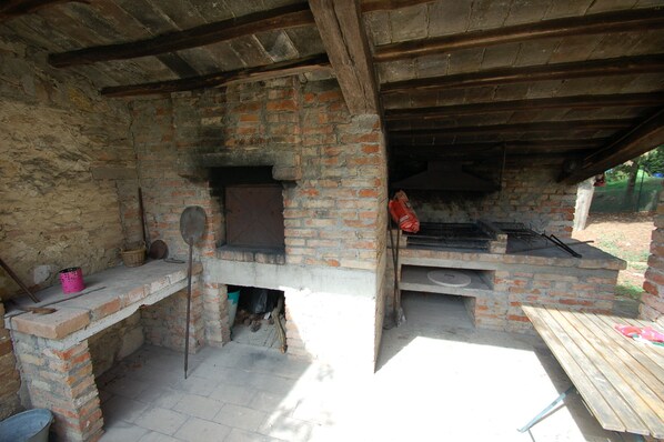 An outdoor brick oven with a chimney, a wooden bench, and a metal bucket. - Detached villa with private pool and fenced garden 30km from Orvieto/Spoleto (Farnetta)