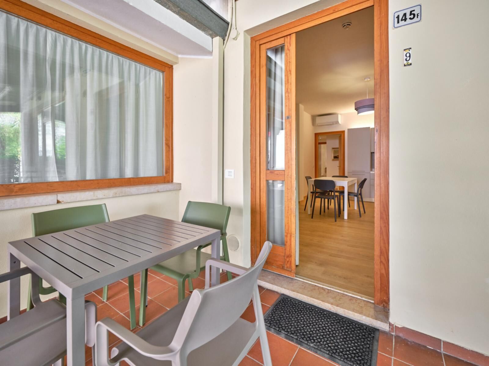 A room with a dining table and chairs, a window with curtains, and a door leading to another room.