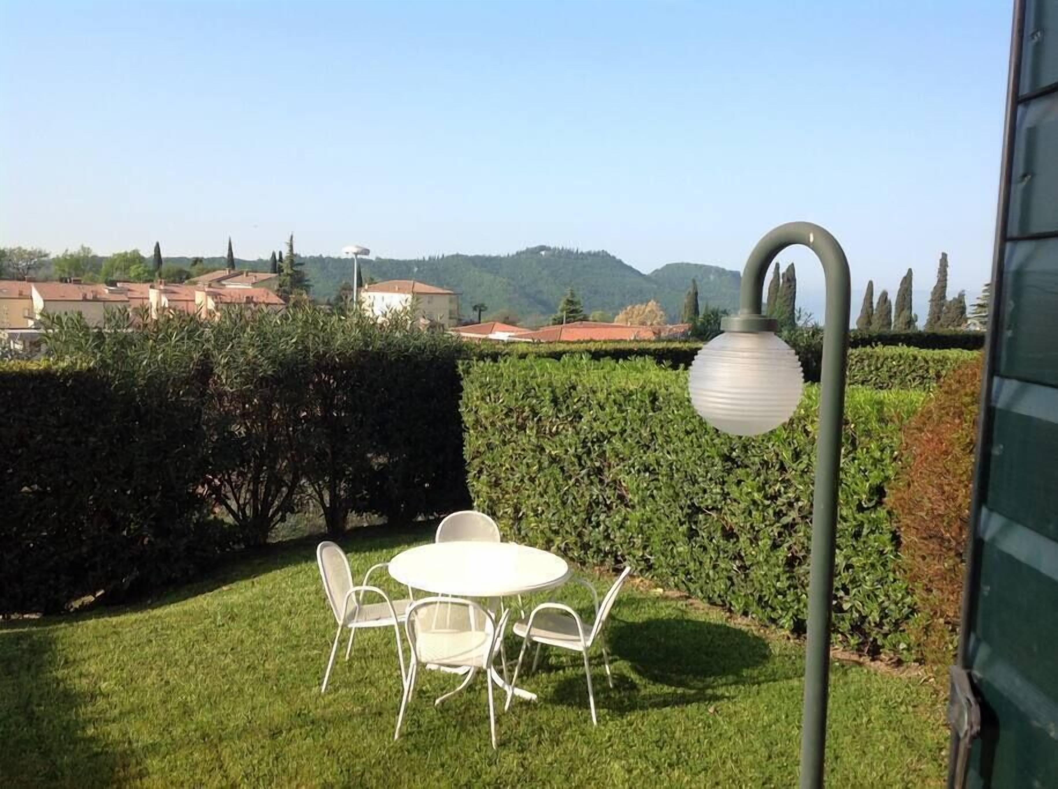Un patio con una mesa redonda y sillas, un farol y vistas a una zona residencial con casas y colinas al fondo.