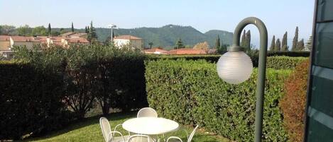 Un patio con una mesa redonda y sillas, un farol y vistas a una zona residencial con casas y colinas al fondo.